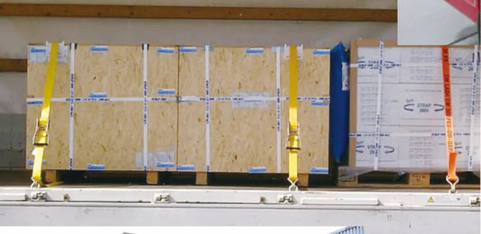 Yellow industrial ratchet straps securing wooden crates and palletized cargo inside a transport trailer